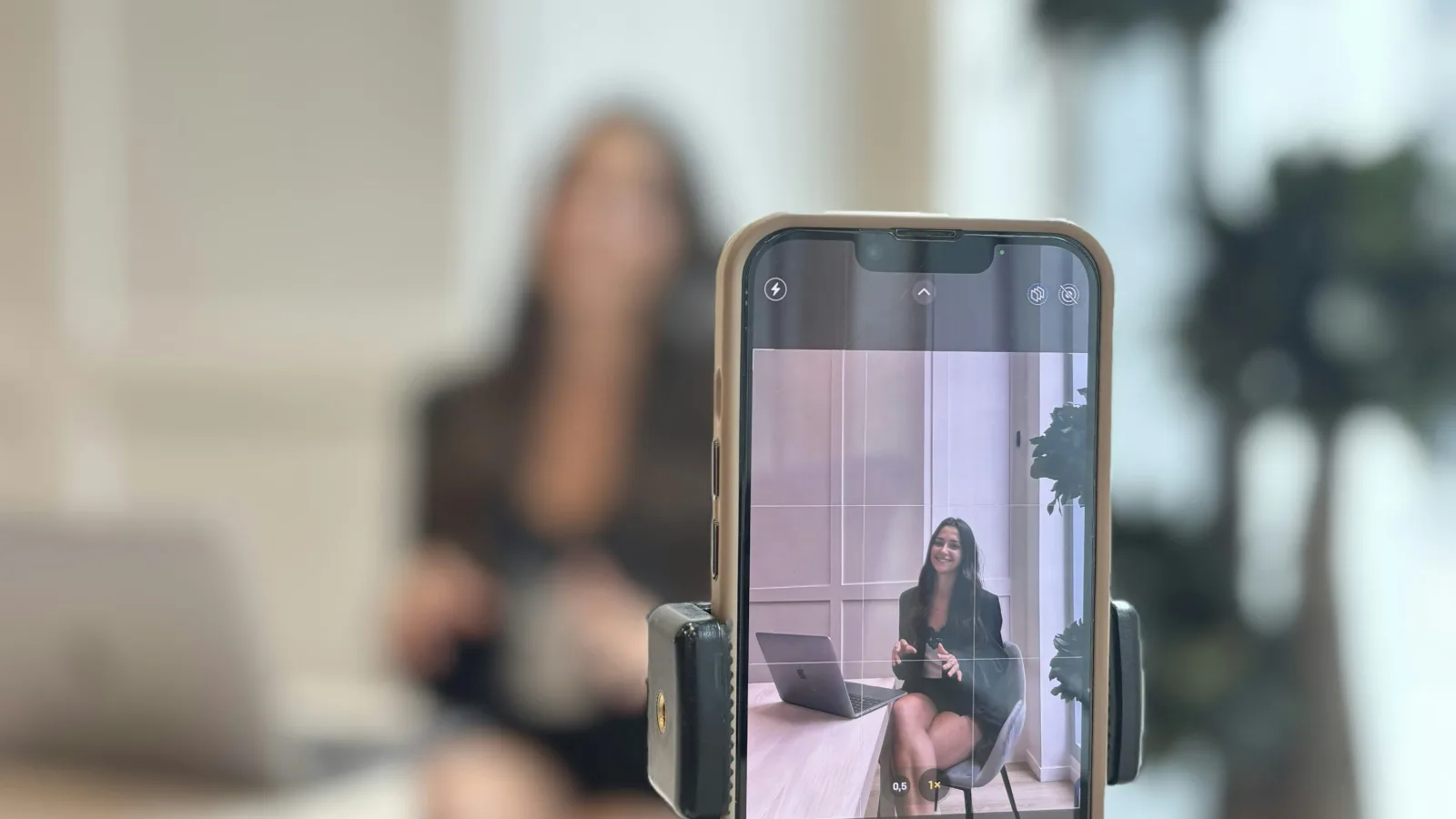 Žena snima video sadržaj pametnim telefonom postavljenim na stativ u uredu.