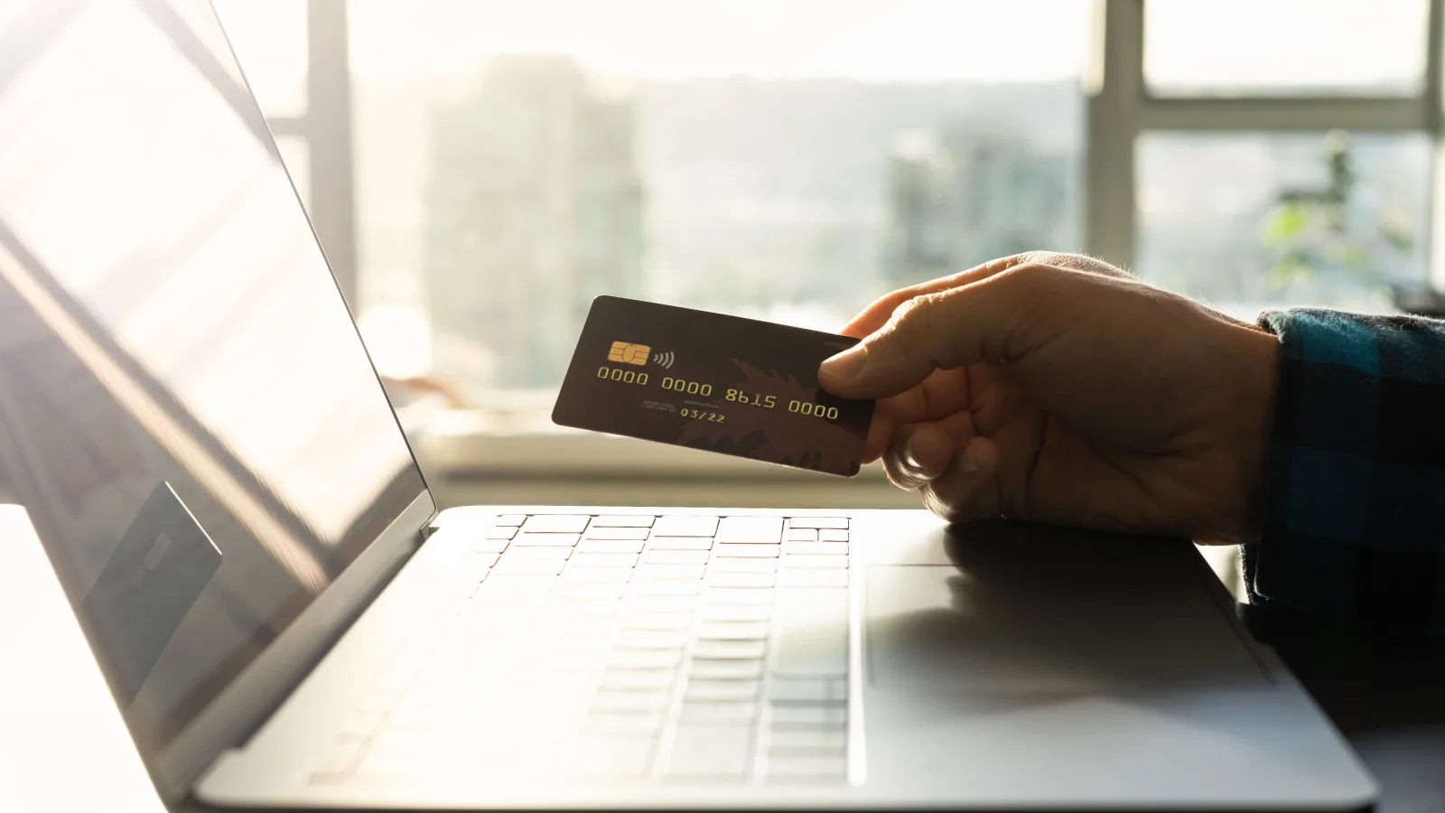 Ruka s kreditnom karticom ispred otvorenog prijenosnika tijekom online kupnje.