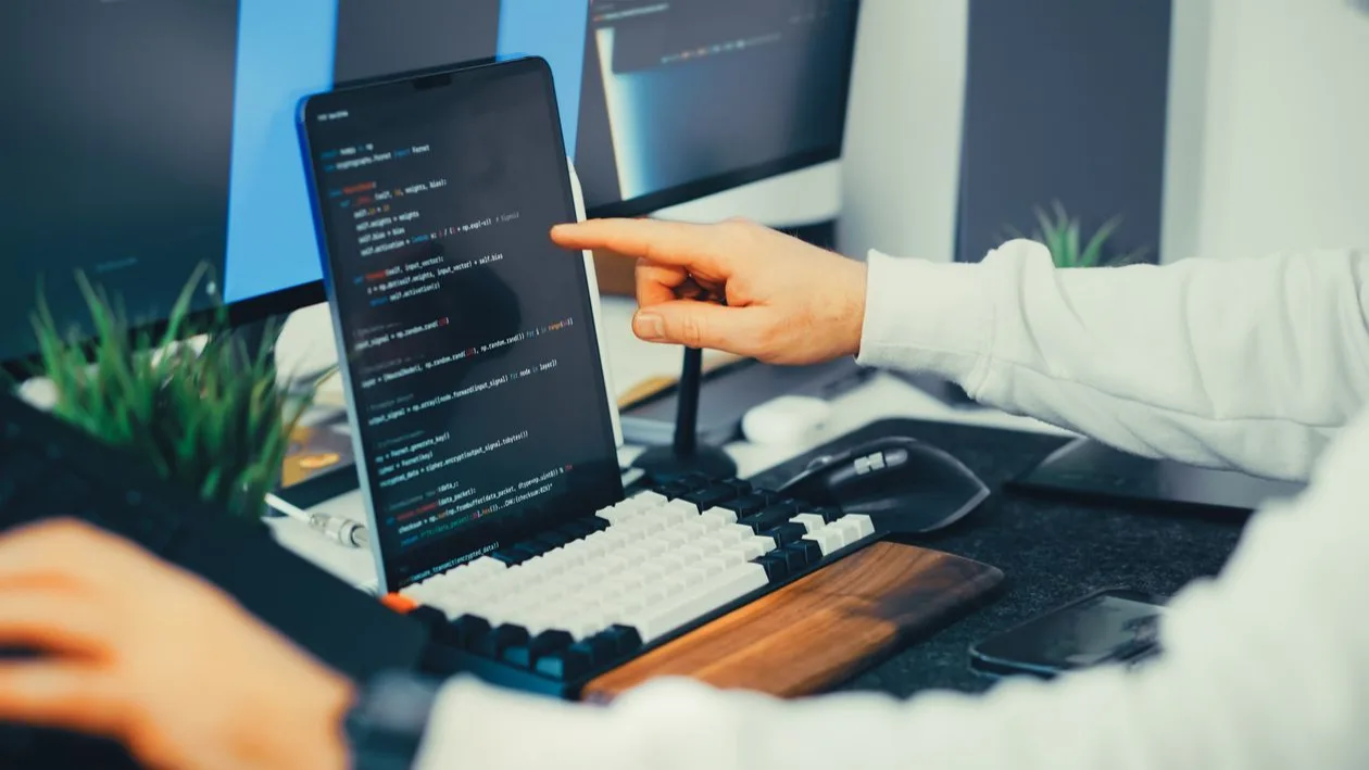 Osoba radi na prijenosnom računalu uz dodatni monitor u uredu.