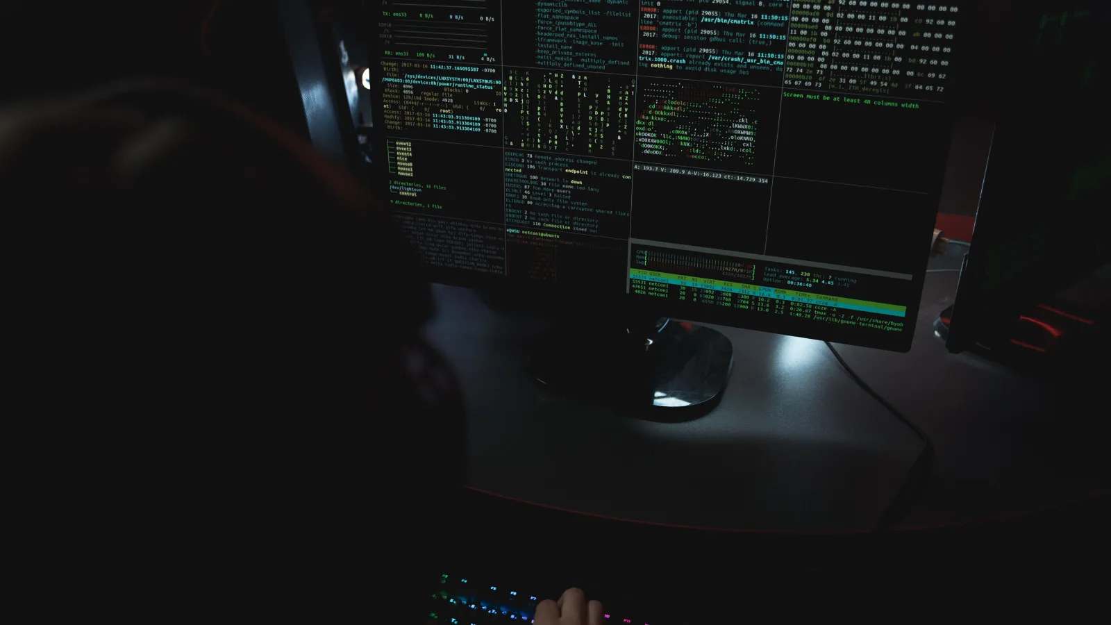 Osoba radi za računalom s više monitora na kojima su otvoreni terminali i programski kod.